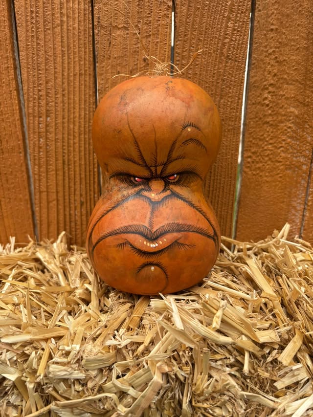 A grumpy orange hand-painted Gourdkin sitting in straw